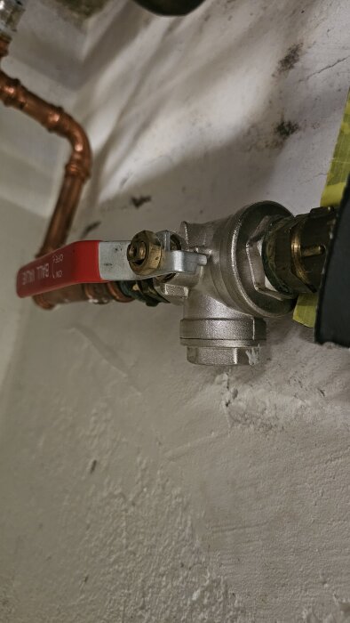 Rött handtag på en kulventil ansluten till ett kopparrör i ett VVS-system.