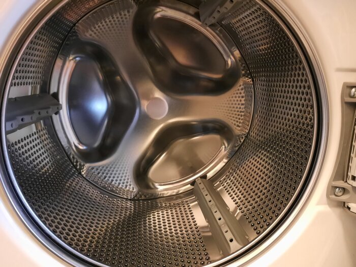 Inuti en tvättmaskinstrumma med metallisk yta och plasthållare.
