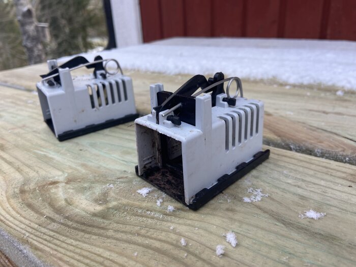 Två musfällor från Biltema placerade utomhus på träplanka med snöflingor runtom.