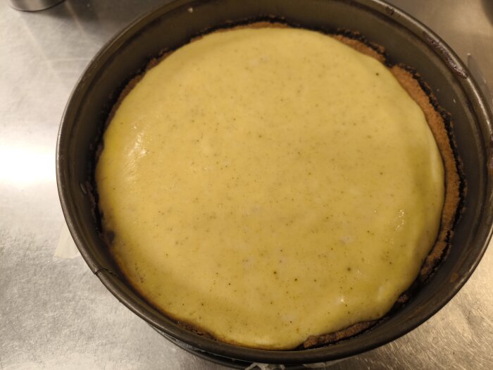 Cheesecake med vaniljfyllning och en Digestive-kexbotten, toppad med italiensk maräng, i springform på ett köksbord.