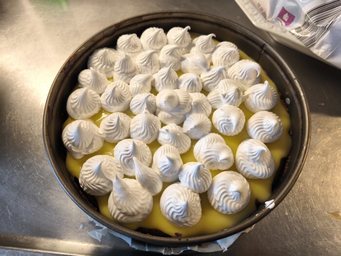 Cheesecake med gul curd och toppad med italiensk maräng i en form på ett köksbord.