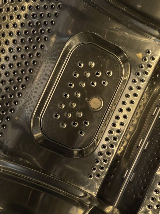 Räddningslucka i en Cylinda-tvättmaskin, monterad på trummans insida med hålmönster.