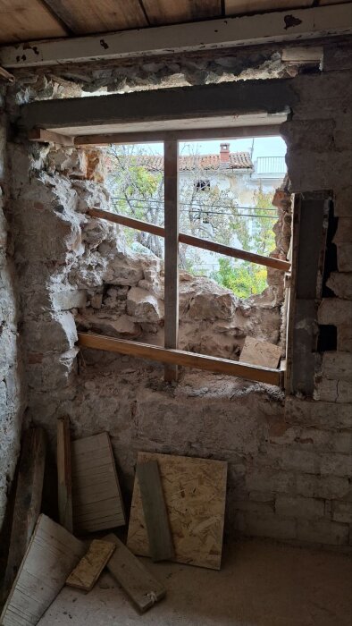 Öppning för nytt fönster i tjock sten- och tegelvägg, brädhög på golvet.
