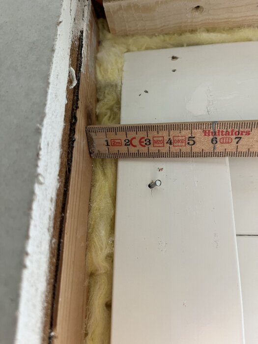 Mätning av avstånd mellan regel och fönsterkarm, markerat med en linjal, visar skillnad mellan 11 mm längst ner och 14 mm högre upp, sett under gipsning.