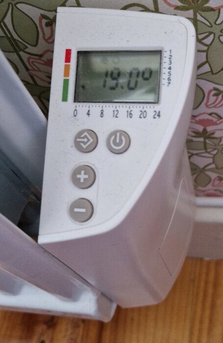 Värmeelementets kontrollpanel med digital display som visar 19°C, knappar och symboler för sol, måne och snöflinga.
