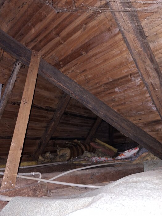 Vind med träbjälkar och plåttak, isoleringsmaterial synligt på golvet.