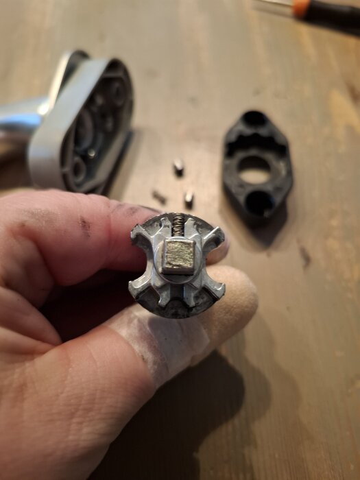 Närbild på en demonterad handtagsmekanism från en altandörr, med en fjäder och små cylinderdelar liggande på ett bord.