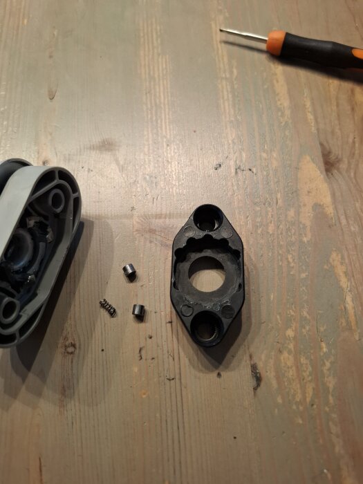 Fjäder och små cylindrar på träbord nära delvis isärtagen låsdel och skruvmejsel.