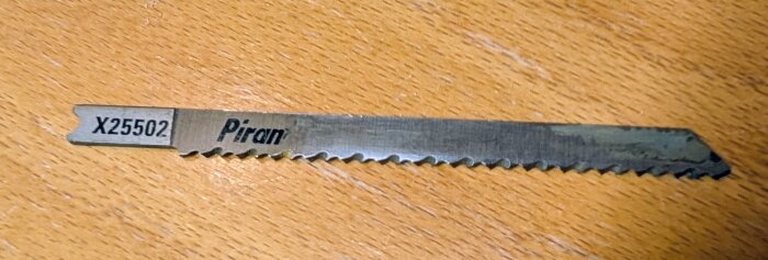 Närbild på ett Piranha-sågblad med märkning X25502, liggande på ett trägolv.