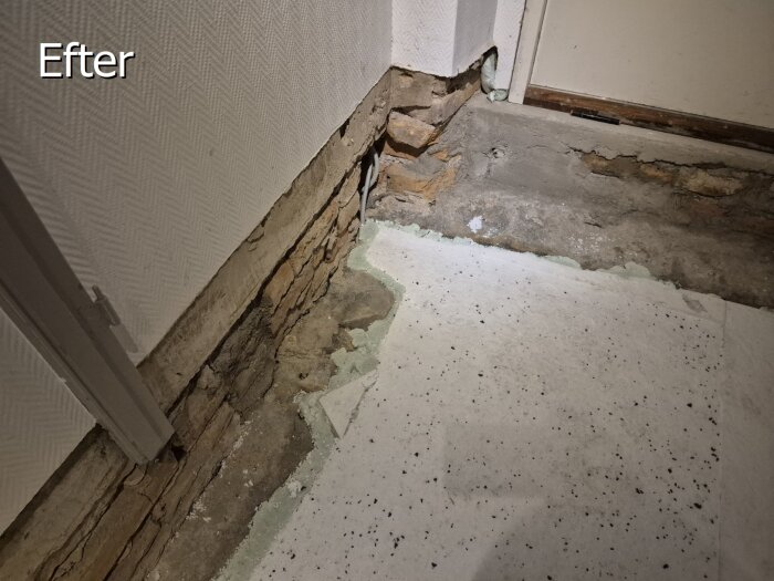 Ojämn vägg med pålagd cellplastgolv, fogskum synligt. Ruggig yta mot väggen där grus och isolering delats. Vägg visar tecken på slitage och reparation.
