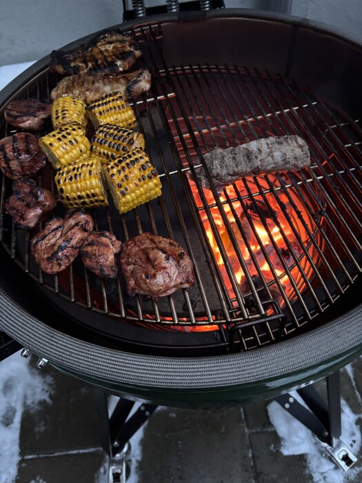 Grill med brinnande kol, majskolvar och kött som grillas.