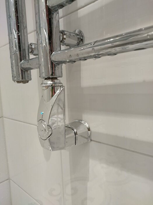 Elektrisk handdukstork med synlig anslutning till väggen, vattendroppar på metallytan tyder på eventuell fuktexponering.