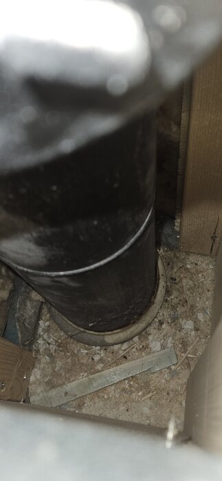 Svart rör på bottenplan av huset, omgiven av betongrester och träplankor. Eventuellt gjutjärn.