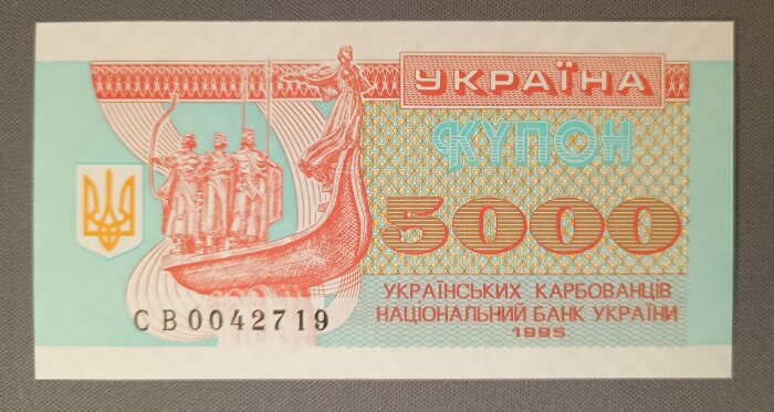 Ukrainsk 5000 karbovanets-sedel från 1995 med illustration av en båt och folk samt Ukrainas statsemblem.