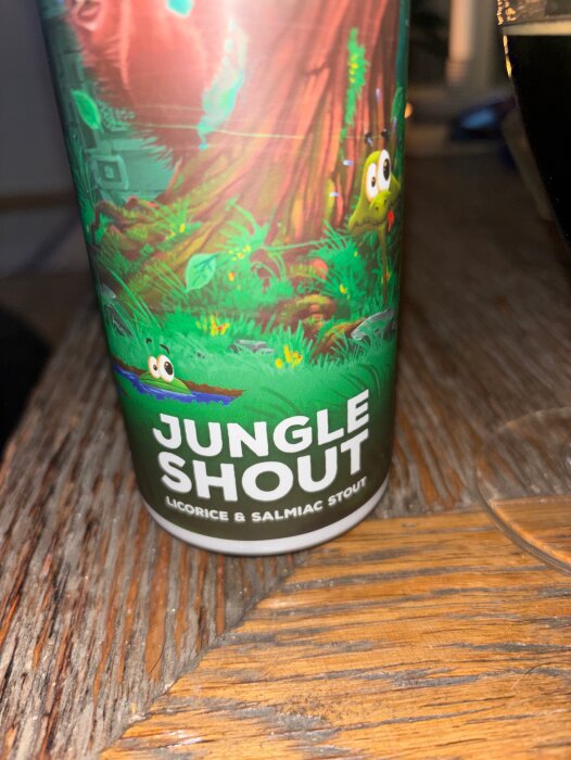 Burk med öl från Benchwarmers Brewing Co, märkt "Jungle Shout", licorice & salmiac stout, står på ett träbord.
