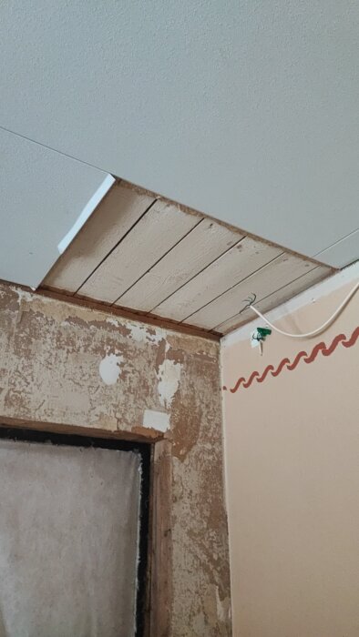 Öppet tak med exponerade träbjälkar och sliten vägg yta under renovering.
