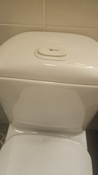 IFÖ toalettstol med en spolarknapp högst upp på cisternen, omgiven av vita kakelväggar.