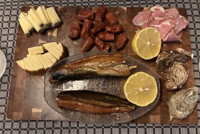 Charkbricka med skinka, ostar, korv, kippers, ostron och citronskivor pÄ en skÀrbrÀda.