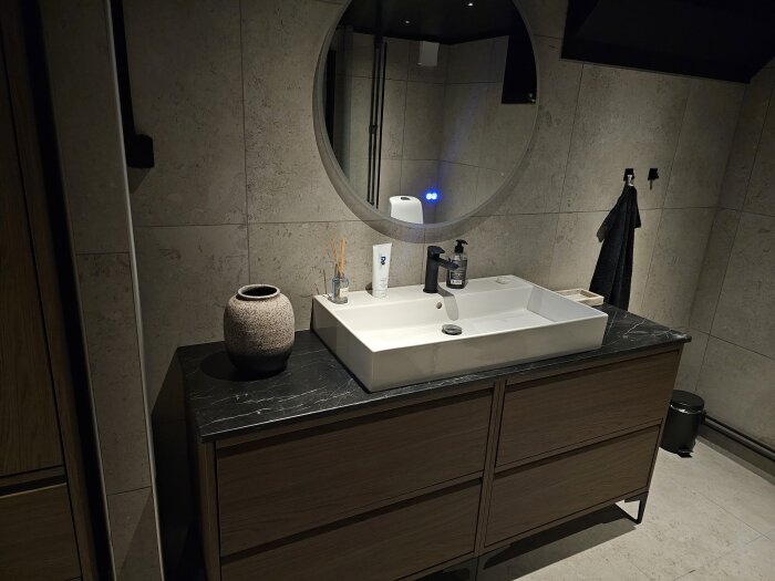 Badrum med svart tak, rund spegel, handfat på svart bänkskiva, enkel dekor och dämpad belysning i källare.