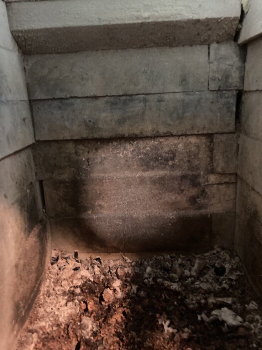 En gammal eldstad med sotiga tegelväggar och aska på botten, cirka 20 år gammal.