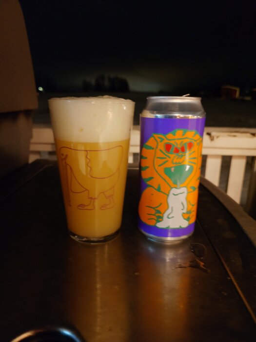 Glas med skummande öl och färgglad Omnipollo-burk på ett bord, mörk bakgrund.