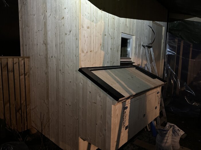 Ommålat trähus med ny träpanel i kvällsbelysning, stege och material synliga intill vägg.