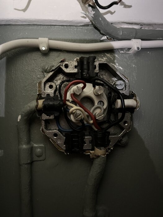 Gammal eldosan med flera färgade kablar, inklusive blå, grå, röd, och svart, samt isolerad tvinad svart kabel upptill.