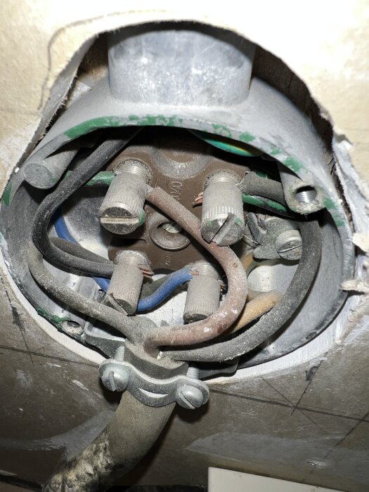 Elcentral med flera kablar och anslutningar, inklusive en synlig blå kabel som kan vara en nolla, omgiven av dammig byggyta.