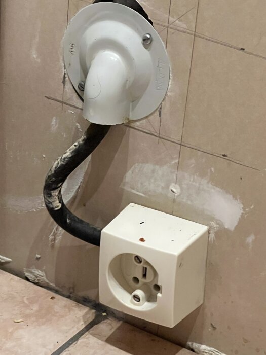 Väggmonterat eluttag och kabel med vit anslutningsbox mot en kaklad vägg, relevant för spisbyte till induktion.