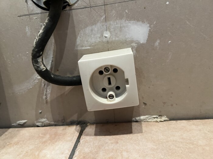 Vägguttag monterat på ljus vägg med synlig elkabel, antagligen för spis, relaterat till fråga om induktionsspis i ett renoveringsprojekt.