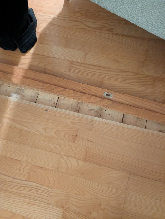 Parkettgolv delvis borttaget, visar träplankor under golvytan, med en skruv som syns på planken.