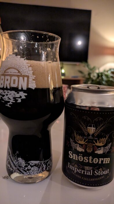 En glas fylld med mörk stout och en burk "Snöstorm Imperial Stout" från Sälens Fjällbryggeri på ett bord.