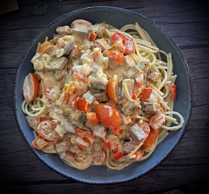 Tallrik med spaghetti och pastasås innehållande fläskfilé, tomater, paprika, lök och sås av lätt crème fraiche, mjölk, sweetchilisås och svartpeppar.