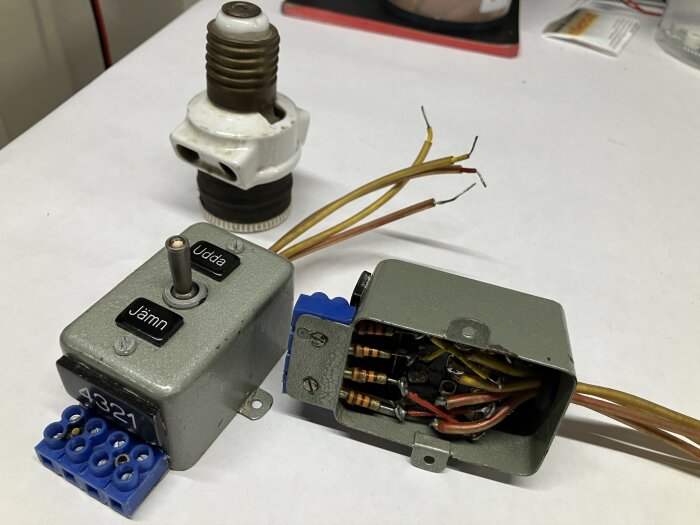 Strömbrytare och kopplingsbox med ledningar, samt en keramisk proppsäkring på ett bord.