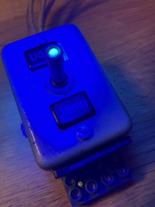 Kontrollbox med blått ljus, två knappar märkta "Udd" och "Jämn" samt en spak, på en träyta.