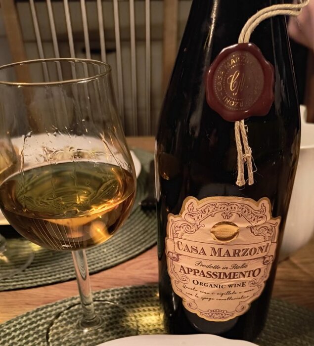 Flaska Casa Marzoni Appassimento-organiskt vin och ett halvfullt vinglas på ett bord med en grön bordstablett.