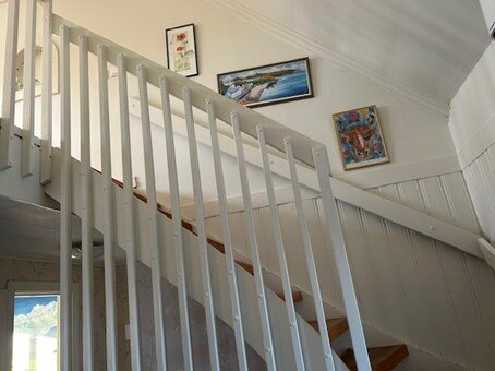 Vit sjuttiotalstrappa med eksteg och högt räcke mot en vägg dekorerad med tre målningar.