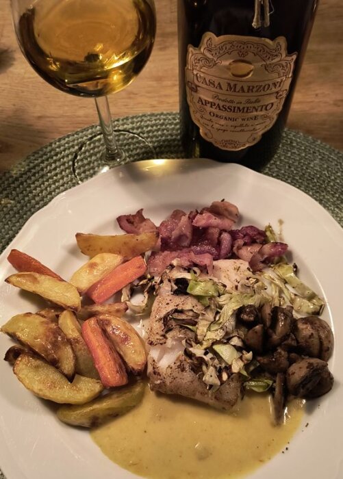 Tallrik med smörstekt torskrygg, bacon, stekta champinjoner, spetskål, potatisklyftor, morötter i ugn och vitvinsås. Glas och flaska vin bredvid.