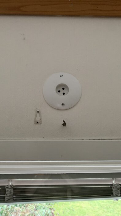 Ojordad lamputtag ovanför fönster på vit vägg, med skruvhål och krok bredvid.