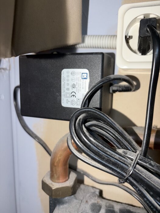Uppkopplat eluttag med adapter och sladdar, bredvid ett kopparrör och en apparatdel i närbild.