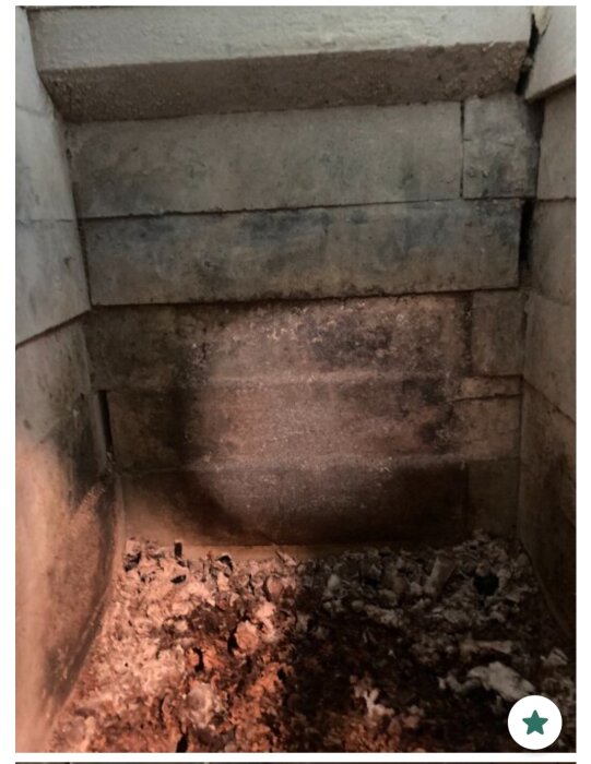 Eldstad med täljstenar, synliga lager utan murbruk eller lera, aska på botten. Vinklad vy visar osammanfogade sidoväggar.