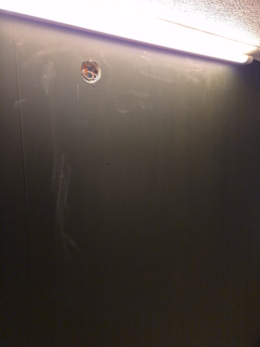 Målad vägg i nyansen Park Green från Rustas Full Matt Edition, med vita märken och en taklampa som lyser upp rummet.