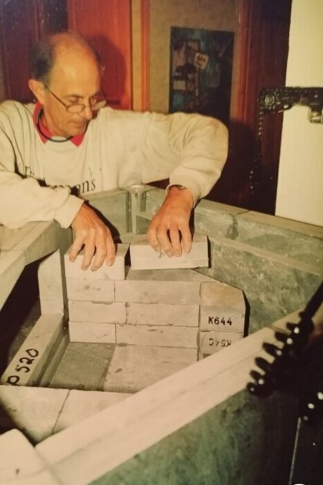 Person placerar täljstenar i eldstad under konstruktion; stenarna verkar inte ha bruk eller lera mellan sig, vilket antyds av diskussionen.