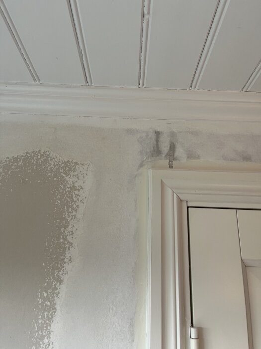 Tapetborttagning vid dörrkarm, där yttre lagret avlägsnats och rester av vitt papper täcker gipsväggen, redo för slipning inför omtapetsering.