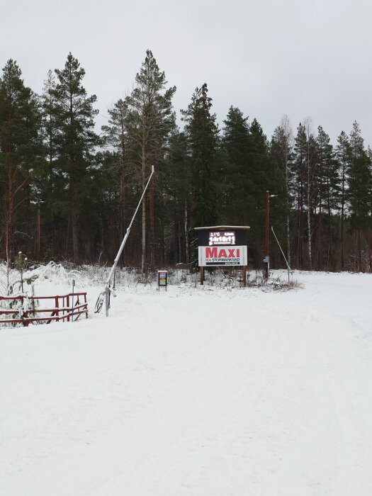 Snöig skog med en skylt för ICA Maxi stormarknad, samt en temperaturskylt, i bakgrunden.