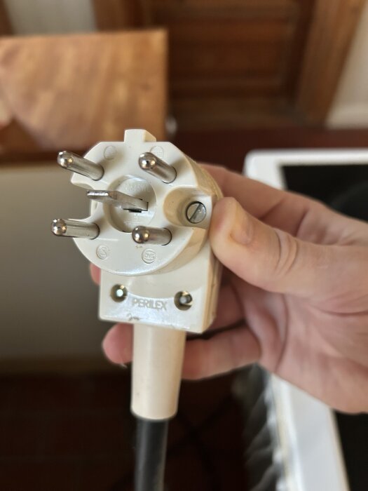 Närbild av en Perilex-kontakt för ett spisuttag, hållen i en persons hand, med fyra stift och en skruv på sidan.