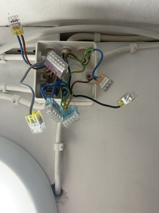 En öppen kopplingsdosa med flera färgkodade kablar och anslutningsplintar monterad på en vägg.