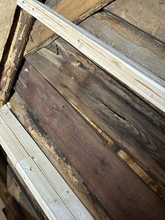 Närbild på innertaket med synliga reglar och träfibermaterial, visar tecken på fuktskador och kondensbildning från tidigare bristande isolering.