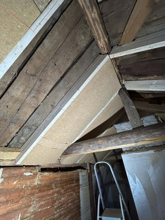 Renoverad övervåning med synliga reglar, isolering och takbjälkar. En stege står uppställd mot väggen.