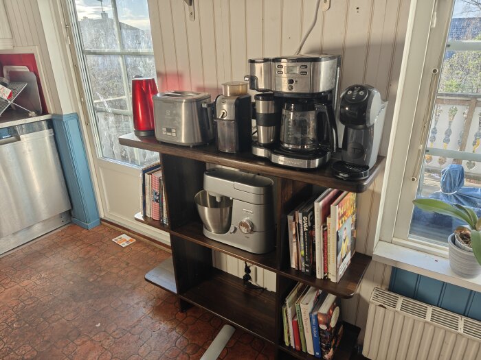 Ny hylla i köket med kaffekokare, brödrost, mixer och kokböcker bredvid ett fönster med utsikt.